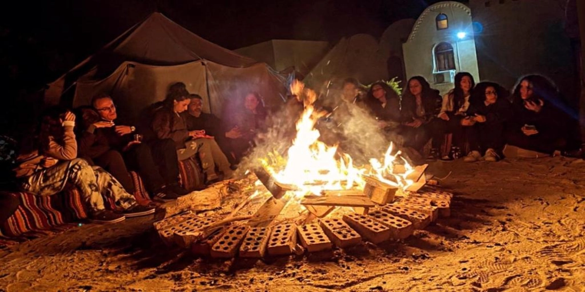 Bedouin camp at night under stars in Egypt’s Black Desert with firelight, tents, and volcanic hills.
