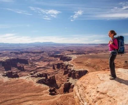 Traveler in desert gear holding water bottle and compass under bright sunlight in Egypt’s sandy landscape.