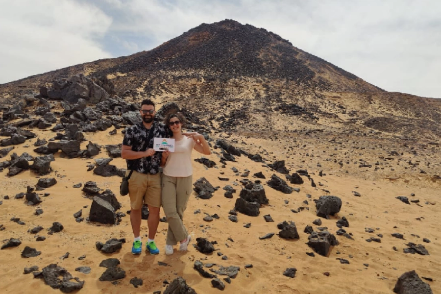 Tourists exploring the Black Desert in Egypt with Heart Egypt Tours, surrounded by black volcanic hills and golden sand dunes at sunset.